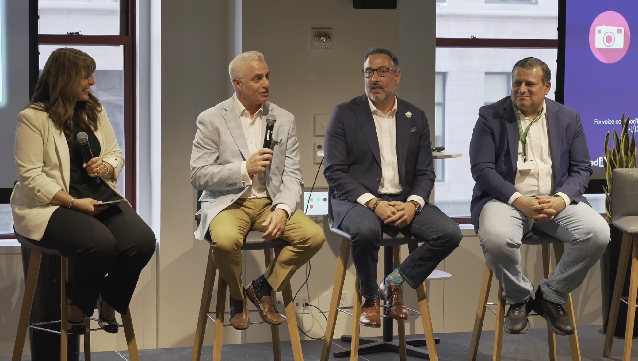 Four panelists seated on stools during a panel discussion, Jonathan Sheppard holding the microphone